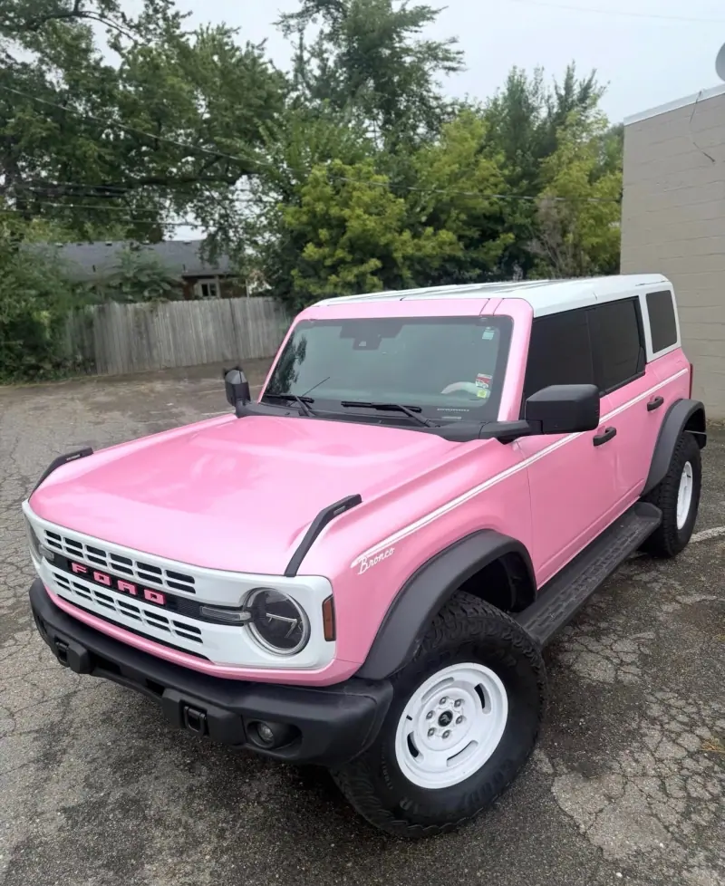 Pink Ford Bronco with a white grille and a white top, front three quarter view