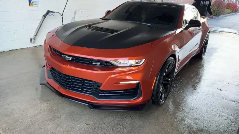 Orange Chevy Camaro SS with a gloss black wrapped hood inside the shop