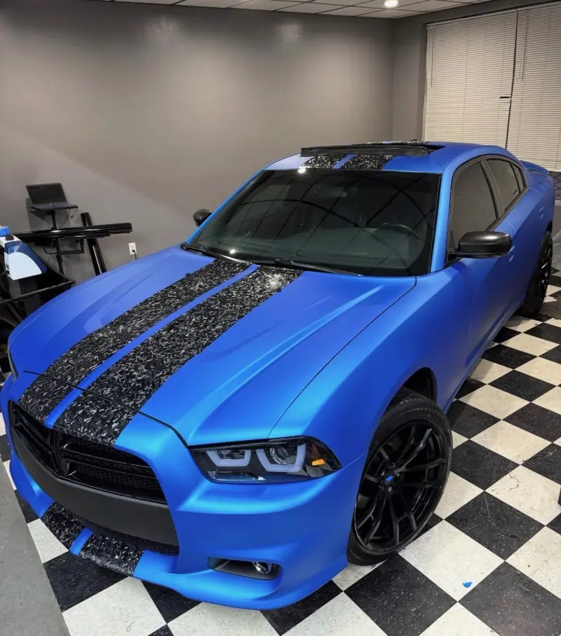 Blue Dodge Charger with forged carbon stripes on a checkered floor, front three quarter view