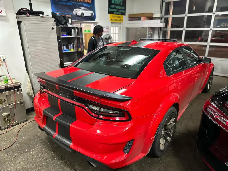 Red Dodge Charger with gloss black racing stripes, rear view inside the shop