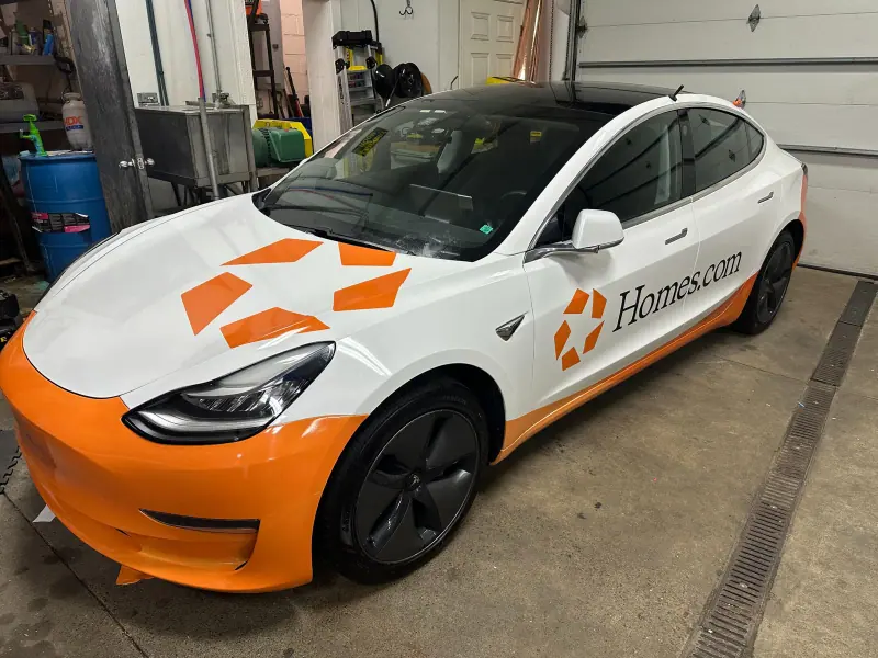Tesla Model 3 in a white and orange Homes.com printed wrap inside the shop
