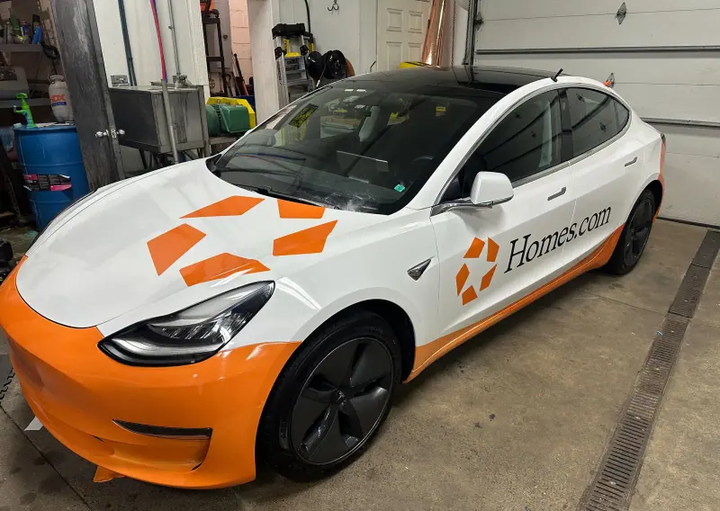 Tesla Model 3 in a white and orange Homes.com printed wrap, front three quarter view inside the shop