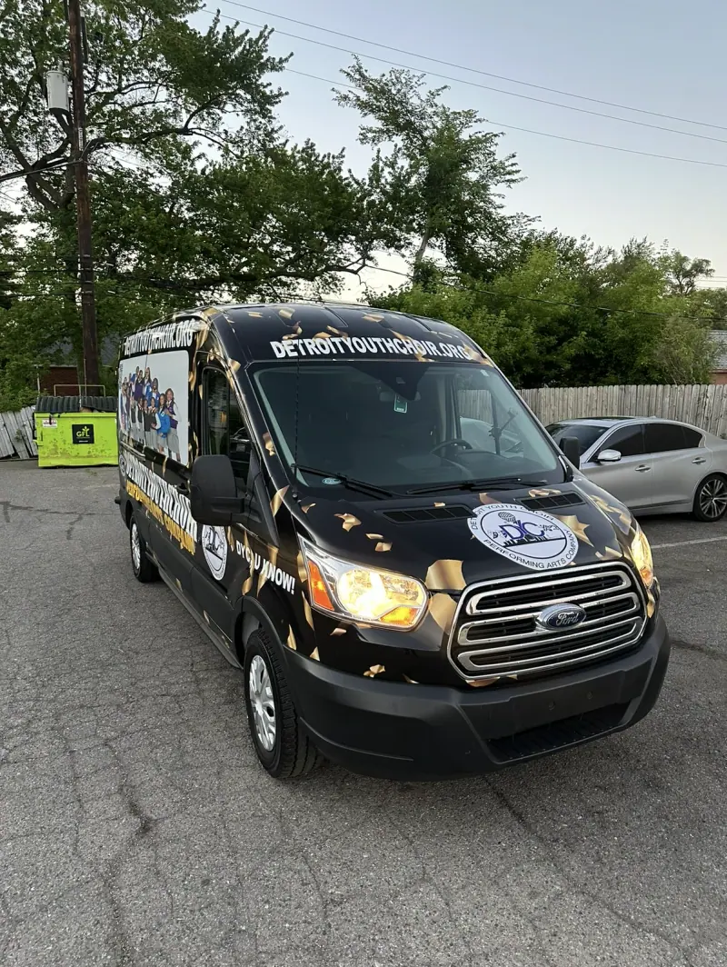 Ford Transit van in a black and gold Detroit Youth Choir printed wrap, front three quarter view
