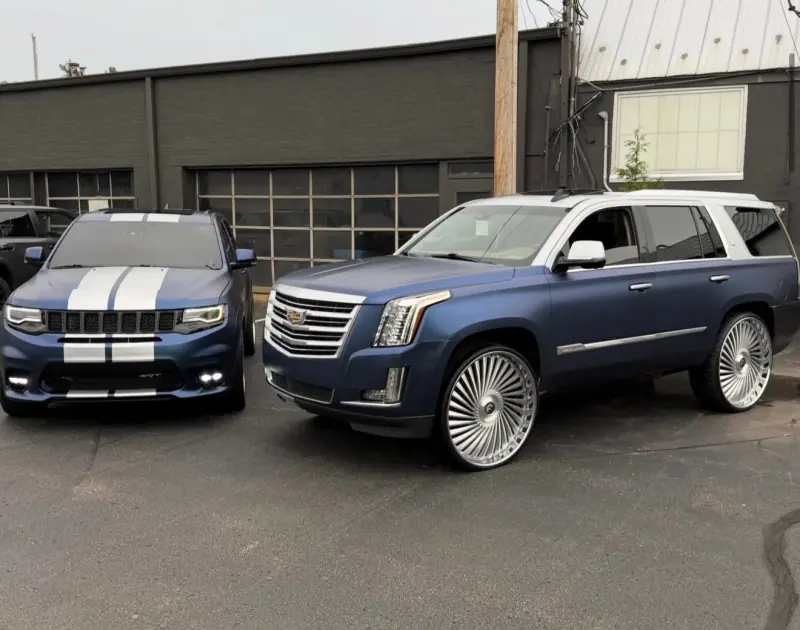 Blue Cadillac Escalade with a white top beside a blue Jeep Grand Cherokee SRT with white stripes