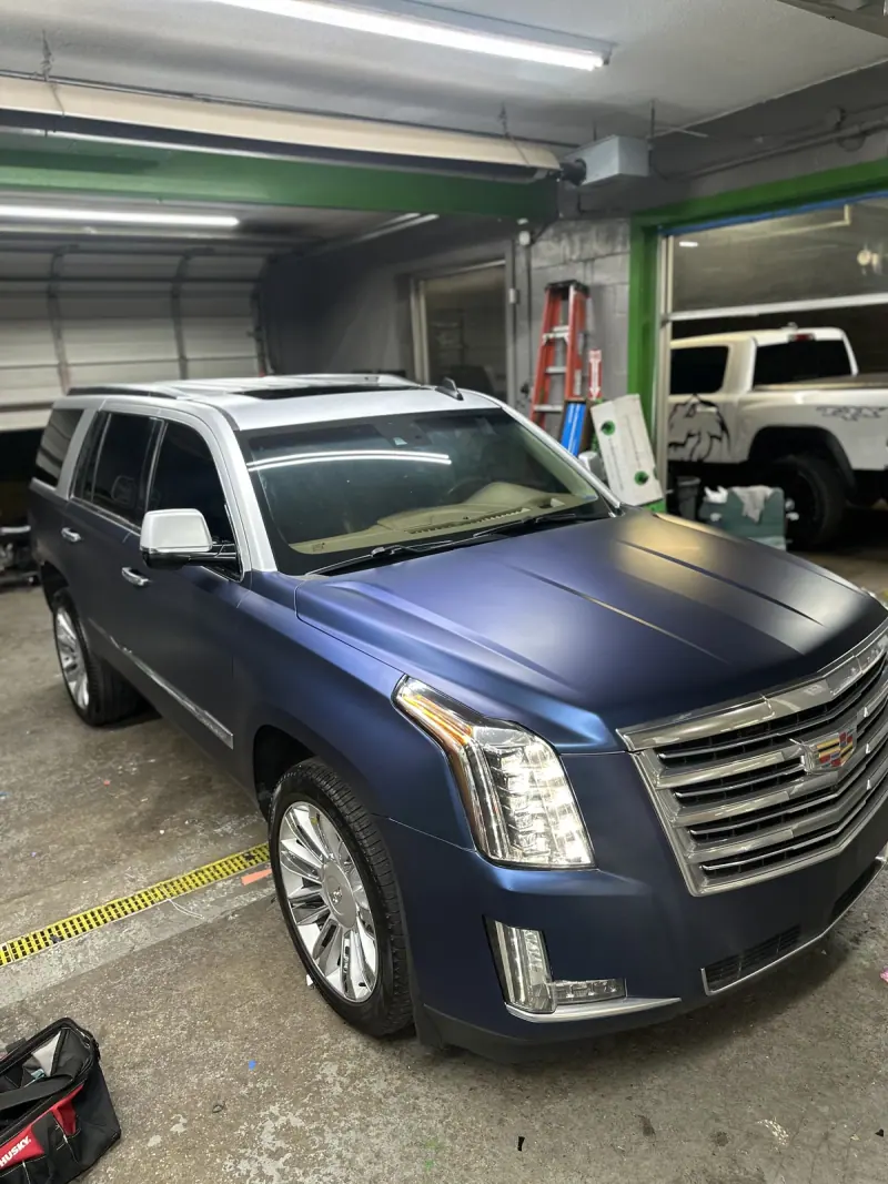 Blue Cadillac Escalade with a white top inside the shop, front three quarter view