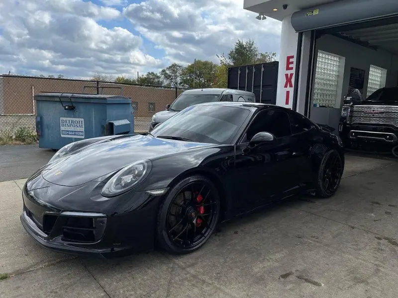 Black Porsche 911, front three quarter view by a garage door