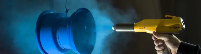 Powder coating gun spraying a wheel in a cloud of blue powder